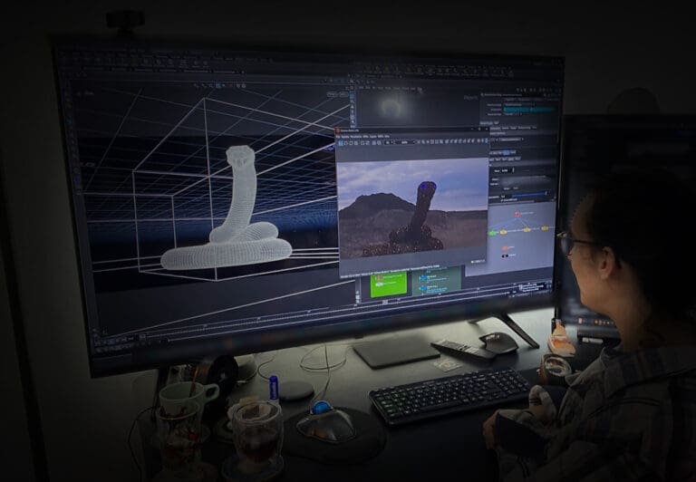 Eline Kouijzer aan haar bureau, met de opgerolde slang in Houdini en een render in Octane op het grote scherm